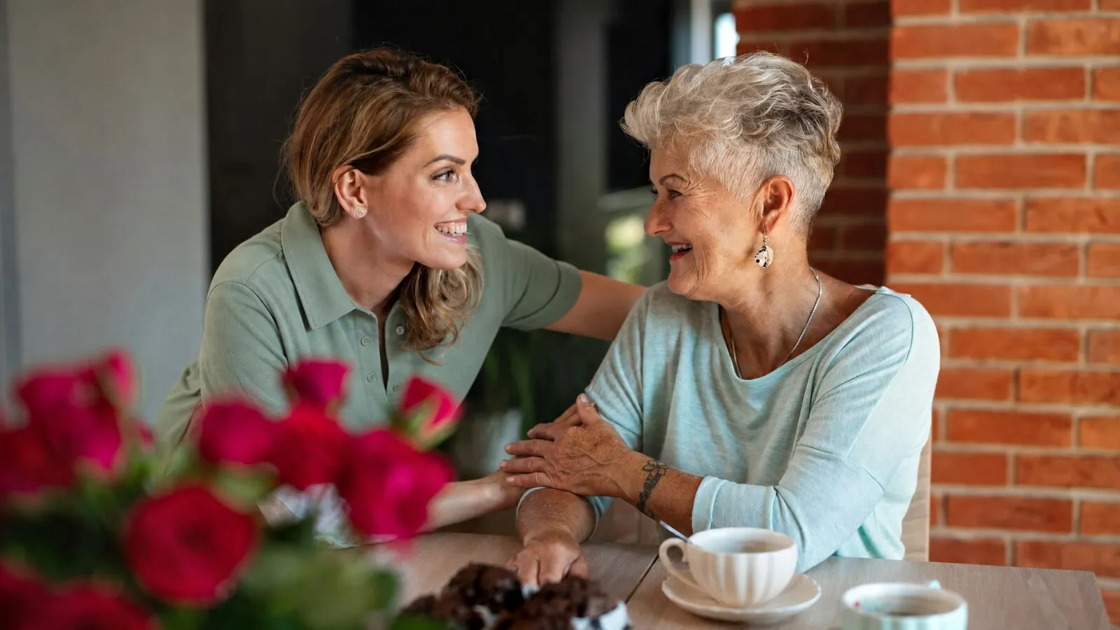 Carer and older woman laughing together over tea
